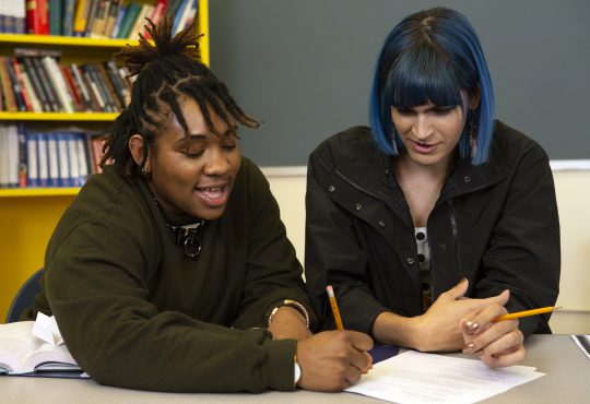 Two non-binary students doing work together in class.