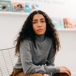 A person sitting in front of a white wall with two shelves of books on the wall