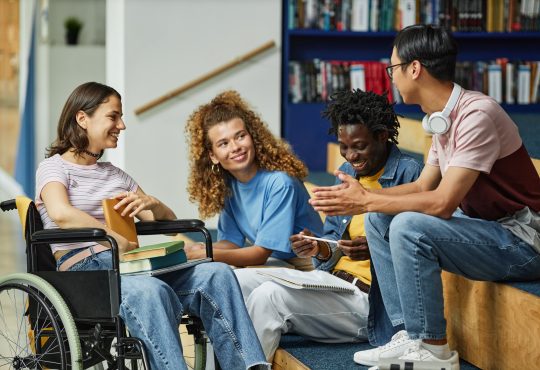 Diverse group of young people chatting in college library including female student with disability